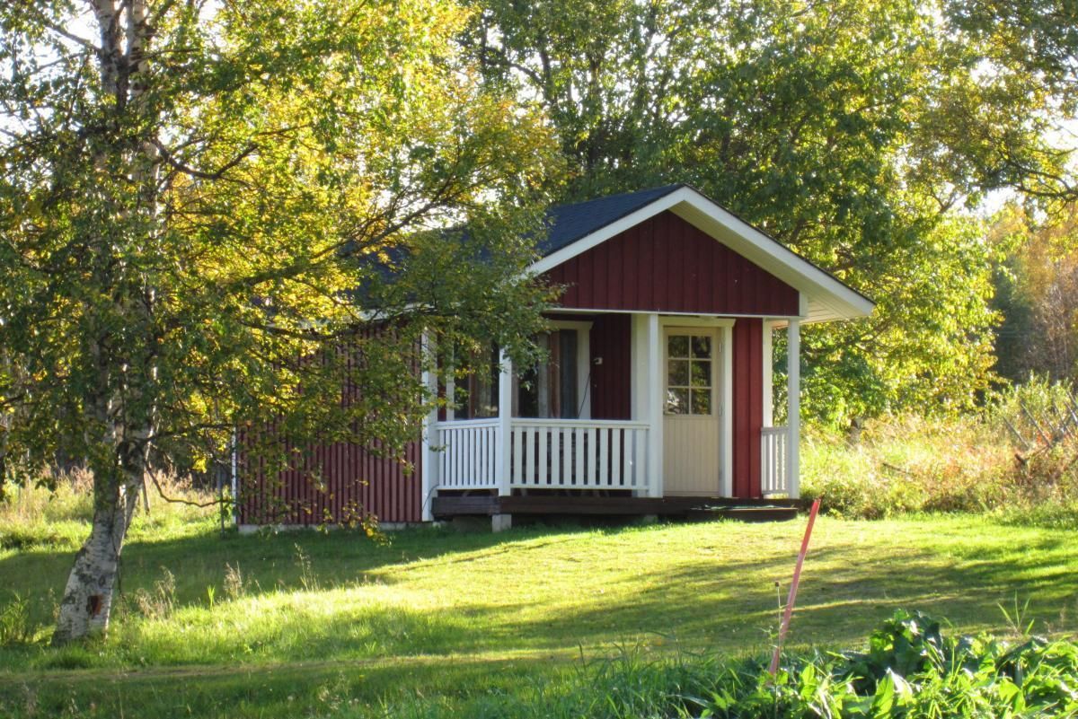 Karpalo-mökki edestäpäin, pieni kuisti valkeilla kaiteilla.