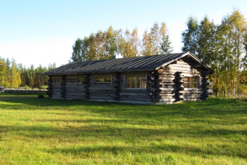Suuri hirsirakenteinen rakennus pihamaisemassa.